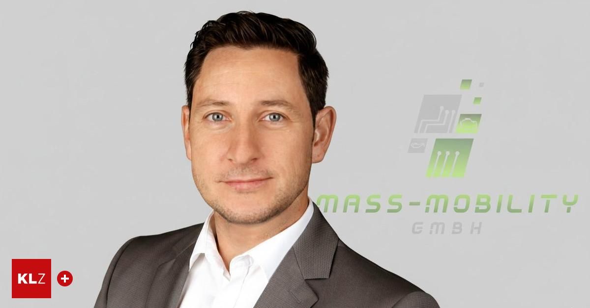 Ein Mann mit kurzen Haaren in einem grauen Anzug und einem weißen Hemd posiert für ein Foto. Hinter ihm befindet sich ein grünes Logo mit dem Text MASS-MOJ GmbH.