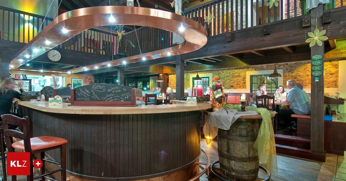 Eine rustikale Kneipe mit einem Kupferbogen und einer Holzbar. Eine Kreidetafel mit Speisekarte steht auf der Theke. Die Leute sitzen an Tischen und ein Fass steht auf der Theke.