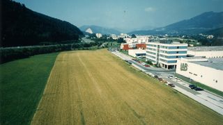 Eine Vogelperspektive eines großen landwirtschaftlichen Feldes, umgeben von einer Stadt, mit einer Autobahn und geparkten Autos im Vordergrund.