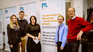 Fünf Personen stehen vor einem Banner, das 100 Jahre Frauen im Bergbau und in der Metallurgie feiert. Zwei Frauen und drei Männer, alle lächelnd und halten Papiere in der Hand.
