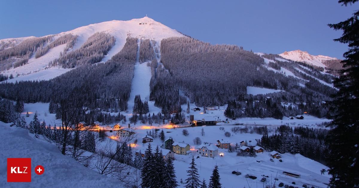 Ein verschneiter Bergdorf mit Kiefern, Häusern und einer Skipiste. Der Himmel ist blau mit einigen Wolken.