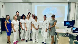 Eine Gruppe von medizinischem Fachpersonal steht vor einer Beamerleinwand, die eine Gehirnscan zeigt. Sie tragen alle weiße Kittel und scheinen zu lächeln.