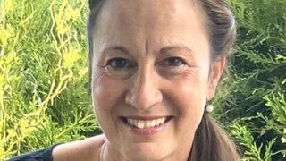 Eine Frau mit einem lächelnden Gesicht steht vor einigen Pflanzen. Sie hat Falten auf ihrer Stirn und um ihre Augen.