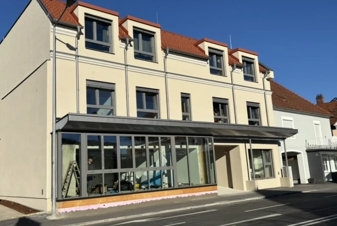 Ein im Bau befindliches Gebäude mit Glasfenstern und -türen steht am Straßenrand.