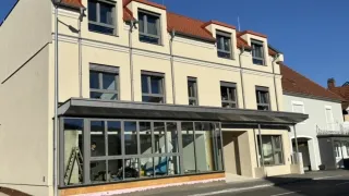 Ein im Bau befindliches Gebäude mit Glasfenstern und -türen steht am Straßenrand.