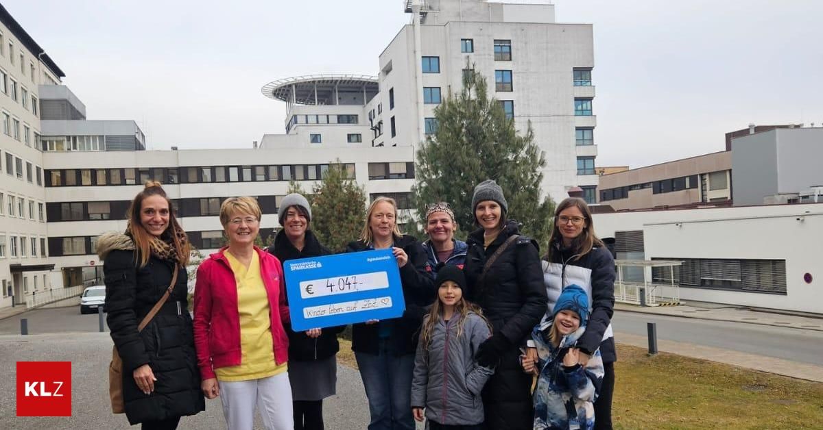 Eine Gruppe von Frauen und Kindern posiert für ein Foto vor einem Gebäude und hält ein blaues Schild mit der Aufschrift 'Spendenabrechnung € 4.047.' Dahinter steht ein hohes Gebäude mit vielen Fenstern und einem Baum.