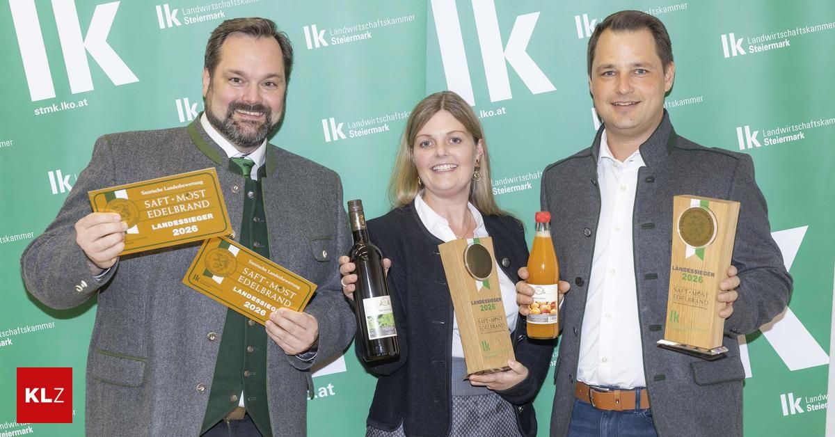 Drei Personen stehen eng beieinander und halten Auszeichnungen, Flaschen und eine Trophäe. Der Mann auf der linken Seite trägt einen grauen Mantel und hält ein Zertifikat. Die Frau in der Mitte hält eine Trophäe und eine Flasche. Der Mann auf der rechten Seite trägt einen grauen Blazer und hält eine Flasche Saft. Hinter ihnen ist ein grüner Hintergrund mit dem Text 'IK Landwirtschaftskammer Steiermark'.