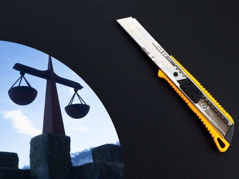 Ein orange-schwarzes Gebrauchsmesser liegt auf einer schwarzen Oberfläche. Dahinter ist eine Silhouette einer Waage der Gerechtigkeit.