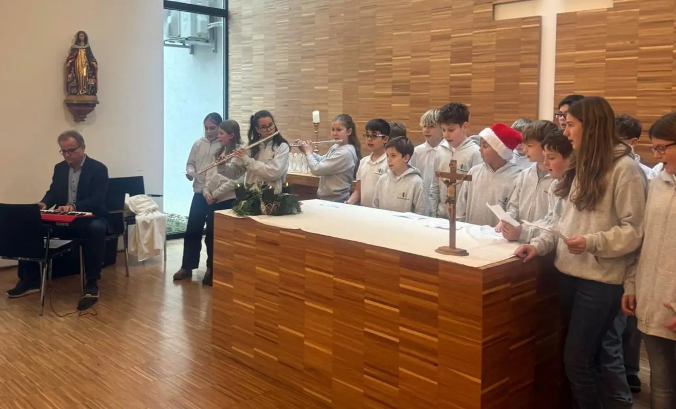 Eine Gruppe von Kindern spielt Flöten in einer Kirche. Sie stehen um einen hölzernen Altar, mit einem Kreuz und Kerzen.