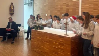 Eine Gruppe von Kindern spielt Flöten in einer Kirche. Sie stehen um einen hölzernen Altar, mit einem Kreuz und Kerzen.