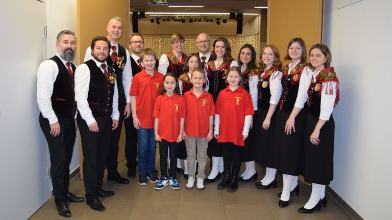 Eine Gruppe von Menschen in roten und schwarzen traditionellen Kleidungsstücken und roten Hemden posiert für ein Foto in einem Raum.