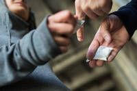 Zwei Personen führen einen Austausch durch. Die Person in Grau gibt der Person in Schwarz etwas. Beide halten kleine Gegenstände in den Händen.