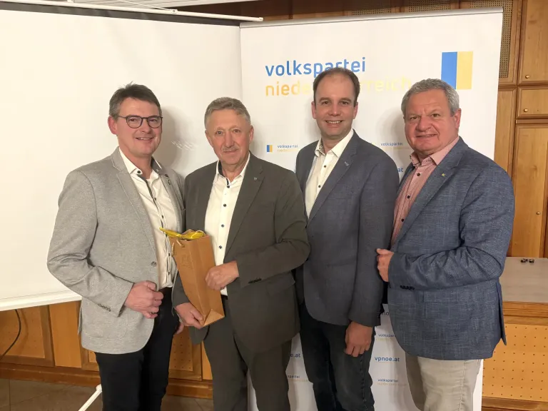 Vier Männer stehen zusammen vor einer Wand mit dem Logo der Volkspartei Niederoesterreich. Ein Mann hält einen braunen Papierbeutel.