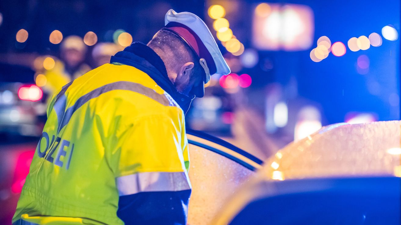 Ein Verkehrspolizist in einem gelben Reflektionsweste und einer weißen Mütze überprüft nachts ein Fahrzeug.