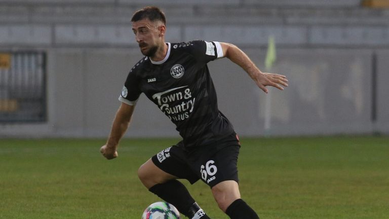 Ein Fußballspieler in einem schwarzen Trikot mit 'Town & Country Haus' und Nummer 66, läuft mit einem Fußball auf dem Feld.