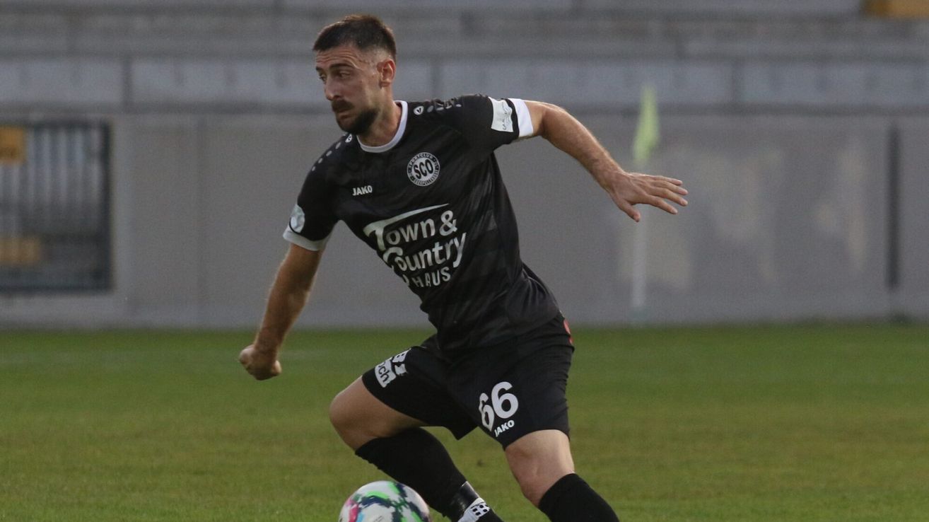 Ein Fußballspieler in einem schwarzen Trikot mit 'Town & Country Haus' und Nummer 66, läuft mit einem Fußball auf dem Feld.