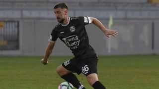 Ein Fußballspieler in einem schwarzen Trikot mit 'Town & Country Haus' und Nummer 66, läuft mit einem Fußball auf dem Feld.