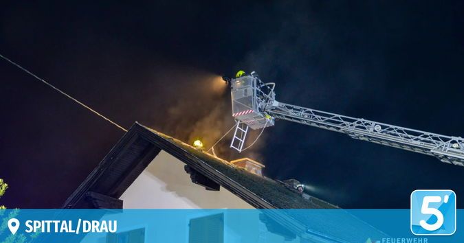 Eine Feuerwehrleiter ist nachts über dem Dach eines Hauses ausgebreitet, mit einem Feuerwehrmann auf der Leiter. Die Szene wird von einem Scheinwerfer beleuchtet.