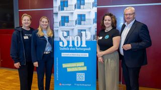Vier Personen stehen neben einem Banner mit der Aufschrift 'STOP. Stadtteile ohne Partnergewalt.' Unten befindet sich ein QR-Code. Die Gruppe scheint für ein Foto zu posieren.