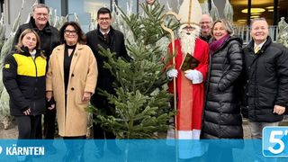 Eine Gruppe von Menschen in Winterkleidung, die lächelnd und für ein Foto mit einem Mann als Sankt Nikolaus und einem Weihnachtsbaum im Vordergrund posiert.