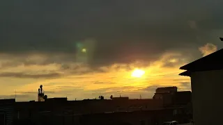 Ein Sonnenuntergang mit gelbem Farbton und Wolken am Himmel, ein kleines Objekt in der Ferne.