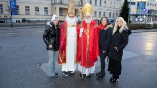 Eine Gruppe von Menschen posiert für ein Foto mit einem Bischof, der als Weihnachtsmann gekleidet ist. Dahinter steht ein Gebäude mit vielen Fenstern.