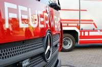 Eine Nahaufnahme eines roten Mercedes-Benz Feuerwehrfahrzeugs, wobei der vordere Stoßfänger und der Kühlergrill deutlich zu sehen sind, geparkt auf einer Straße.