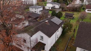 Ein Luftbild einer Nachbarschaft mit Häusern, einige mit Solarpanelen auf ihren Dächern. Bäume und Sträucher umgeben die Häuser.