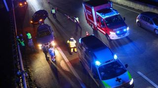 Eine Luftaufnahme einer Straße mit mehreren geparkten Autos. Ein Feuerwehrwagen ist mit blinkenden Lichtern auf der Seite geparkt. Eine Person steht auf dem Bürgersteig, und eine weitere ist in der Nähe des Autos.