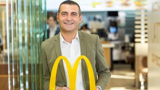 Ein Mann lächelt vor einem McDonald's-Schild und hält einen gelben Buchstaben M in den Händen.