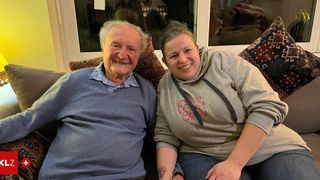 Ein älterer Mann und eine junge Frau lächeln und sitzen auf einem Sofa, wahrscheinlich im Wohnzimmer.