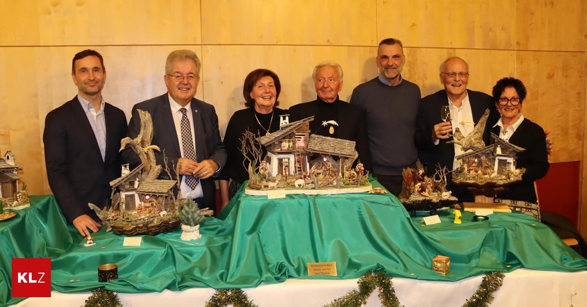 Eine Gruppe von Menschen steht um einen Tisch mit einer Weihnachtskrippe darauf, lächelt und hält Weingläser in der Hand.