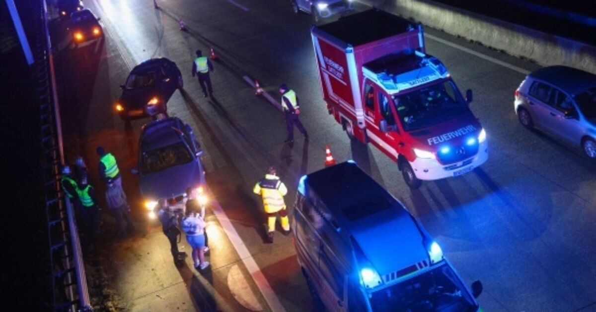 Rettungsfahrzeuge und Personal sind an der Unfallstelle auf einer Autobahn in der Nacht. Fahrzeuge sind geparkt, und Verkehrskegel sind aufgestellt.