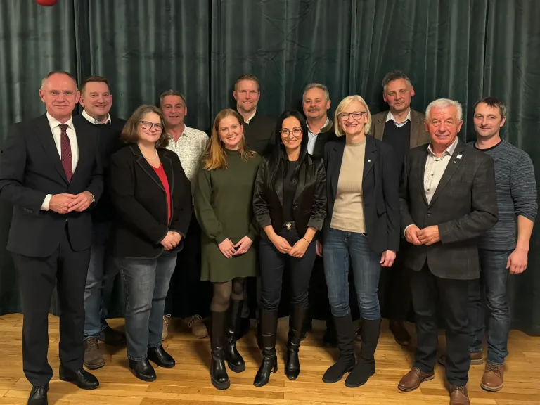 Eine Gruppe von Menschen posiert für ein Bild in einem Raum mit Holzboden. Sie sind formell gekleidet.