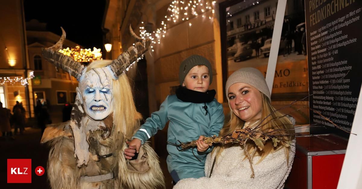 Eine Frau und ein Kind in Kostümen posieren mit einer Person in einer Hornmaske. Sie sind draußen bei Nacht, mit einem Gebäude und einem gerahmten Bild im Hintergrund.