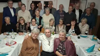 Eine große Gruppe älterer Personen posiert für ein Foto in einem gut beleuchteten Raum. Einige sitzen an einem Tisch, während andere dahinter stehen. Sie alle lächeln für die Kamera.