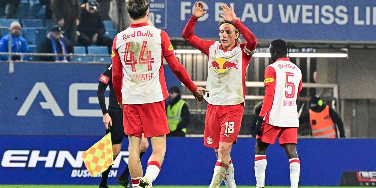 Fußballspieler feiern auf dem Spielfeld mit einer blauen Wand im Hintergrund. Spieler 18 hebt beide Hände. Die Spieler tragen Trikots mit den Nummern 44 und 5.