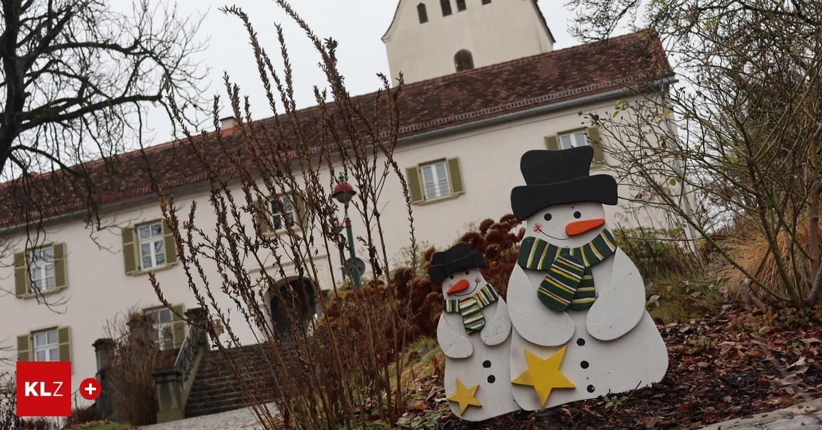 Zwei hölzerne Schneemänner mit Schals und Mützen stehen vor einem Haus mit braunem Dach.