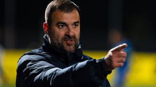 Ein Mann mit Bart und Schnurrbart in einem schwarzen Jackett zeigt mit der Hand eine Richtung an.