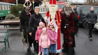 Eine Familie mit drei Kindern steht mit dem Weihnachtsmann, zwei Krampus-Figuren und einem weiteren Mann im Hintergrund.