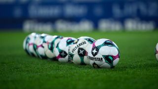 Eine Reihe von Derbystar-Fußballbällen auf einem Rasenfeld, mit einem unscharfen Hintergrund.