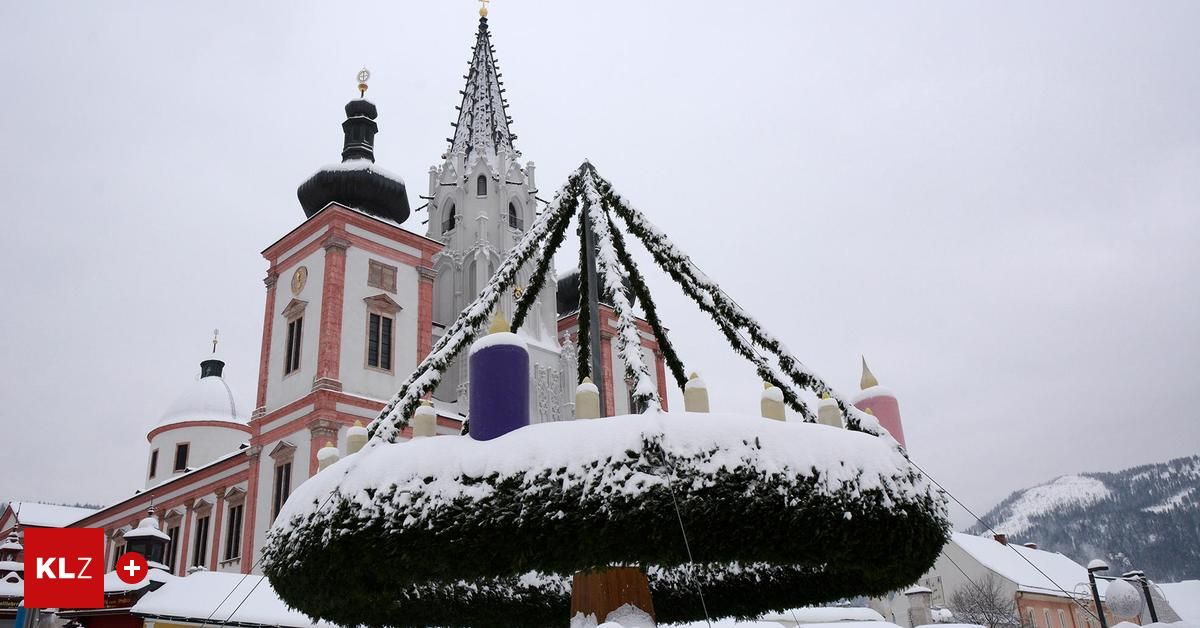 Eine Kirche mit Schnee bedeckt und davor ein kreisförmiger Kranz, der mit Kerzen verziert ist.