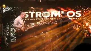 Eine Band auf der Bühne mit einem Gitarristen, einem Schlagzeuger und einem Sänger, alles unter einem großen Banner mit dem Text 'Stromio'.