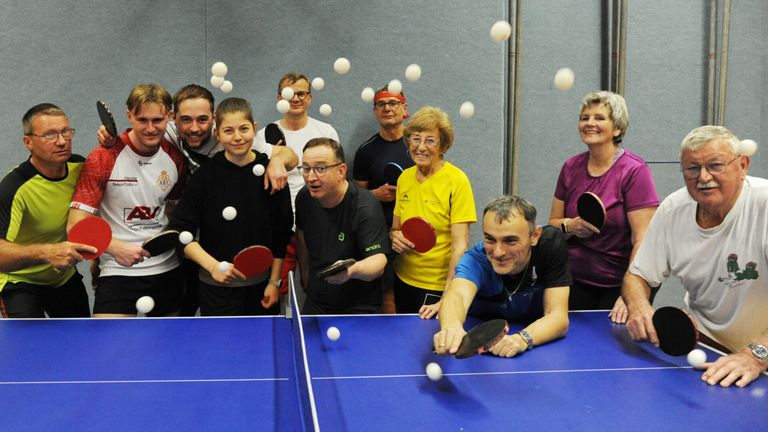 Eine Gruppe von Menschen posiert für ein Foto beim Tischtennisspielen, mit mehreren Tischtennisbällen in der Luft.