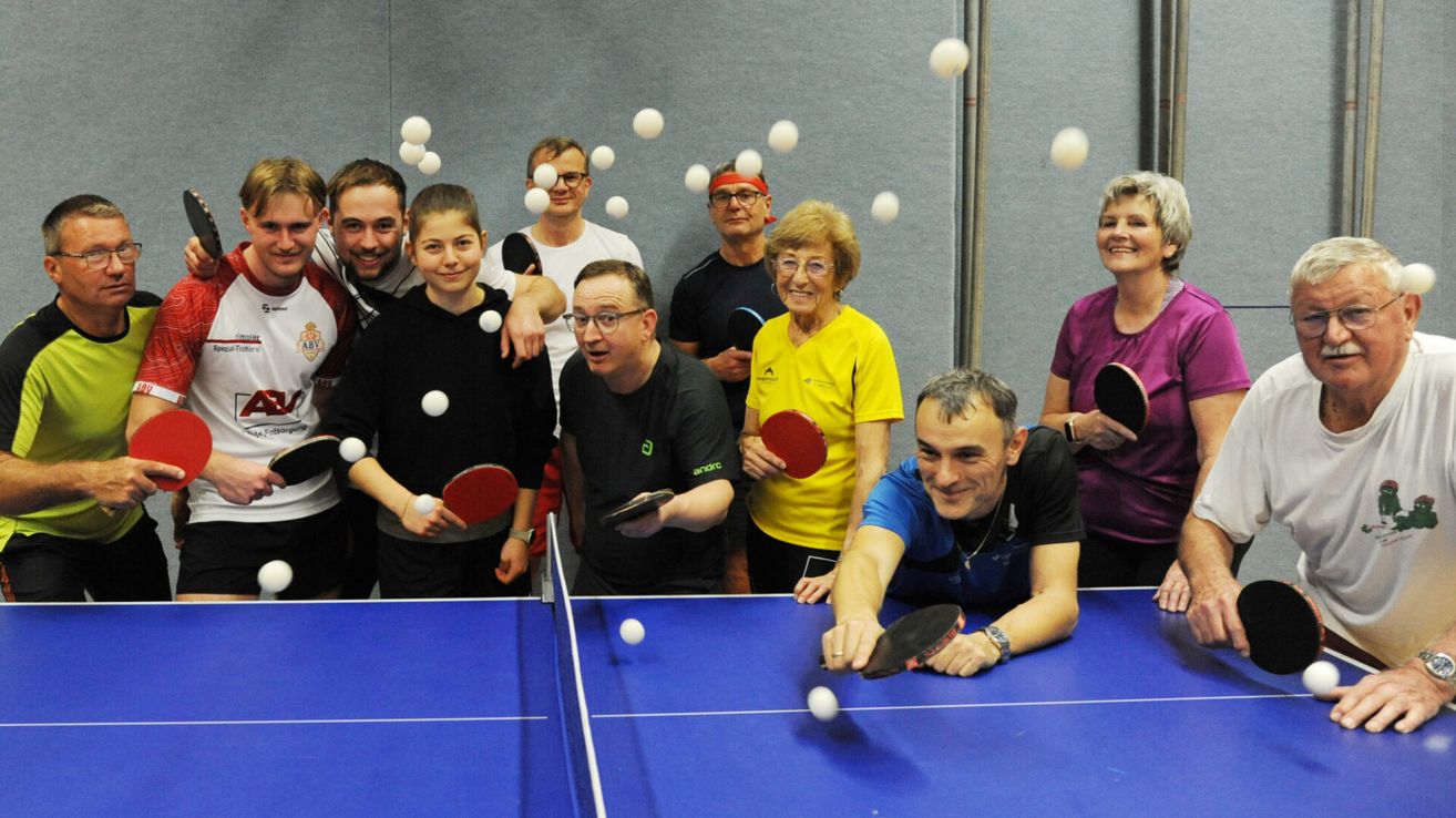 Eine Gruppe von Menschen posiert für ein Foto beim Tischtennisspielen, mit mehreren Tischtennisbällen in der Luft.