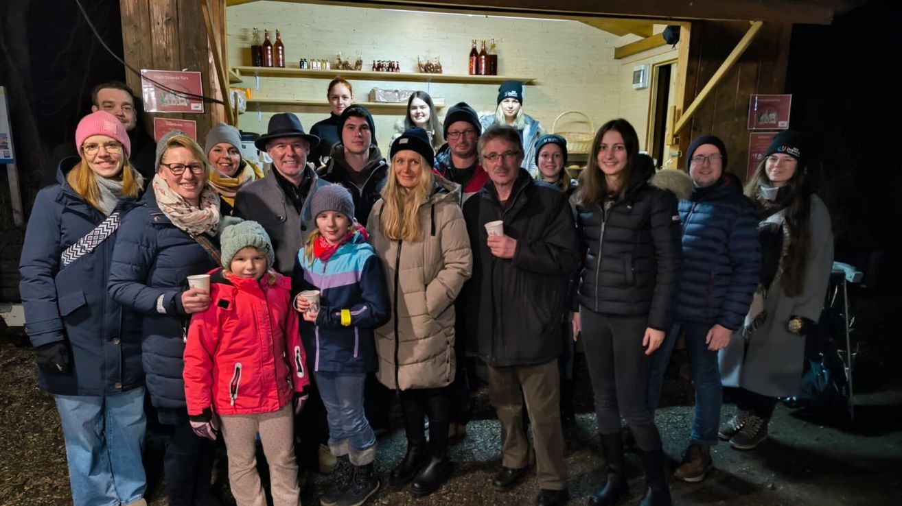 Eine Gruppe von Menschen, darunter Erwachsene und Kinder, posiert für ein Foto in einem Raum mit Holzwänden und Regalen voller Flaschen.