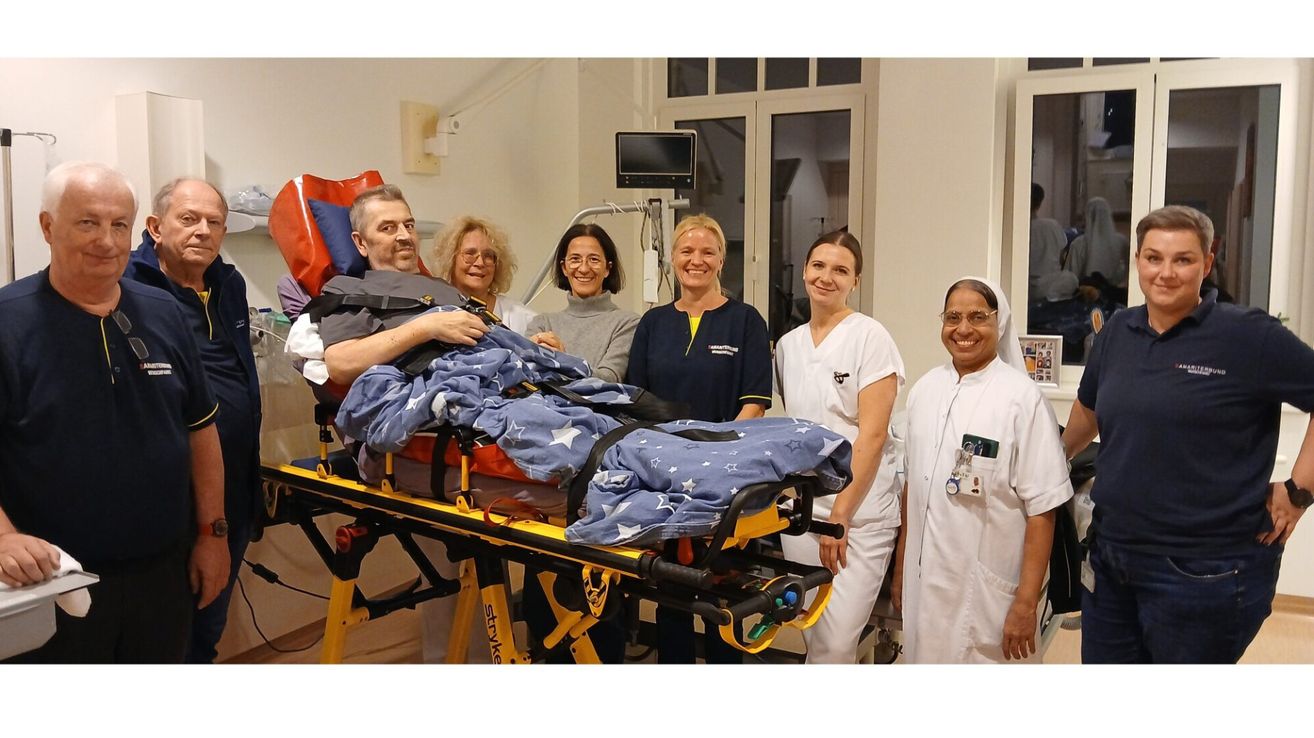 Eine Gruppe lächelnder medizinischer Fachkräfte umgibt einen Patienten im Krankenhausbett, lächelt und posiert für ein Foto.