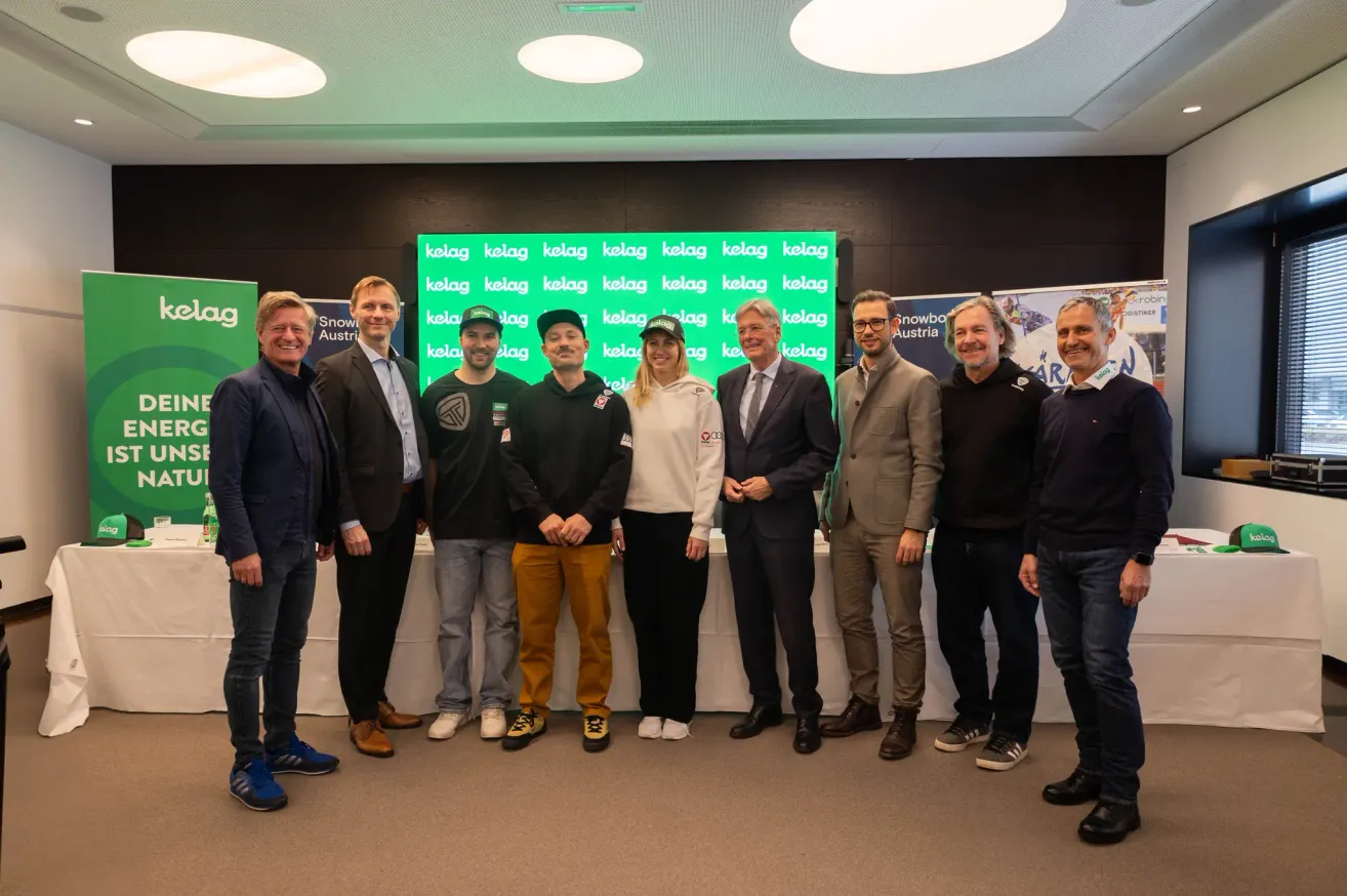 Eine Gruppe von Personen, die formell gekleidet sind, posiert für ein Foto vor einem grünen Hintergrund mit dem Wort Kelag. Sie lächeln und scheinen sich auf einer Veranstaltung zu befinden.