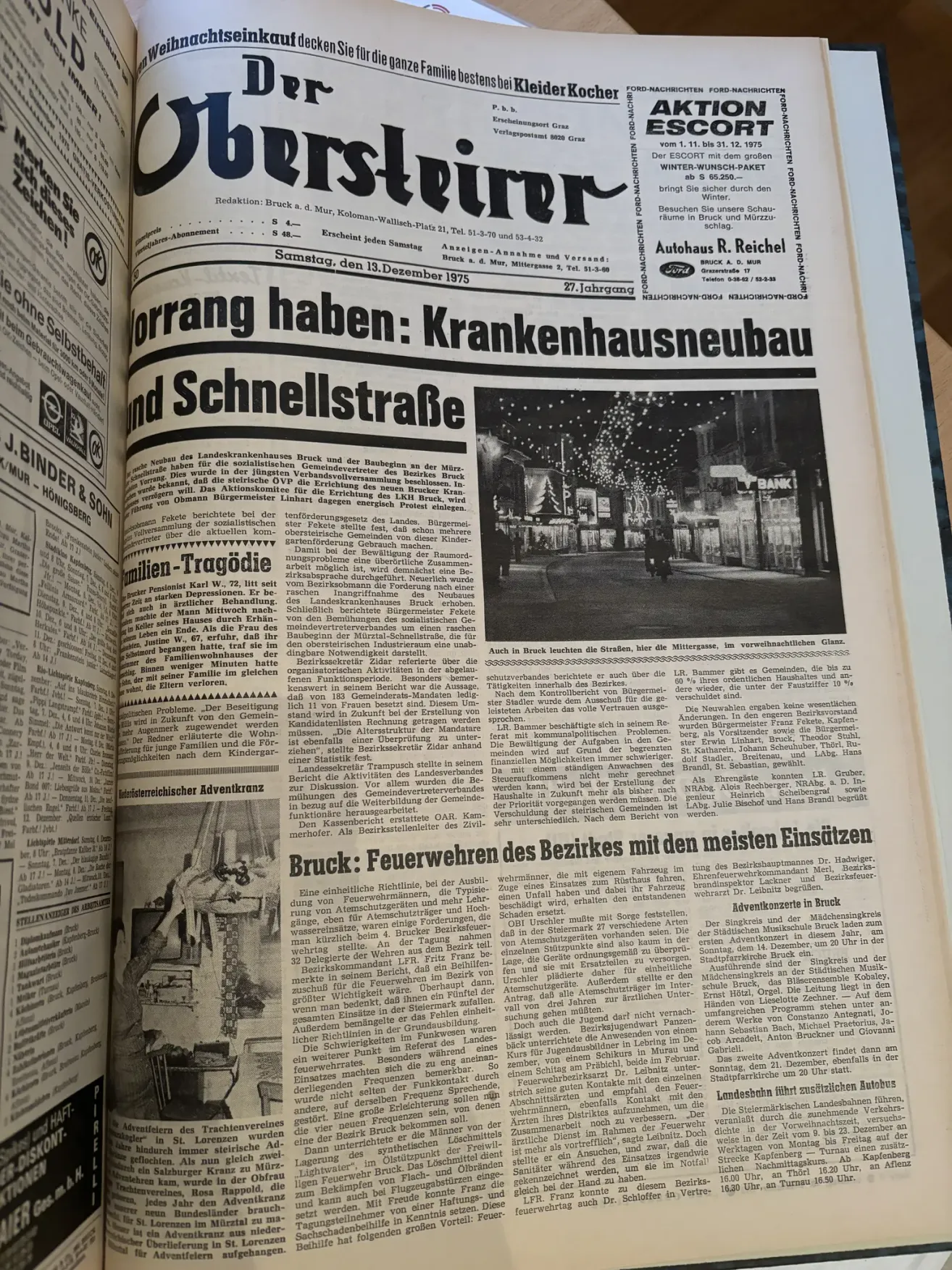 Geöffnete Zeitung mit einem Artikel über den Neubau eines Krankenhauses. Das Foto zeigt eine beleuchtete Straße bei Nacht mit gehenden Personen. Ein weiterer Artikel handelt von einem Ereignis der Feuerwehr im Bezirk.