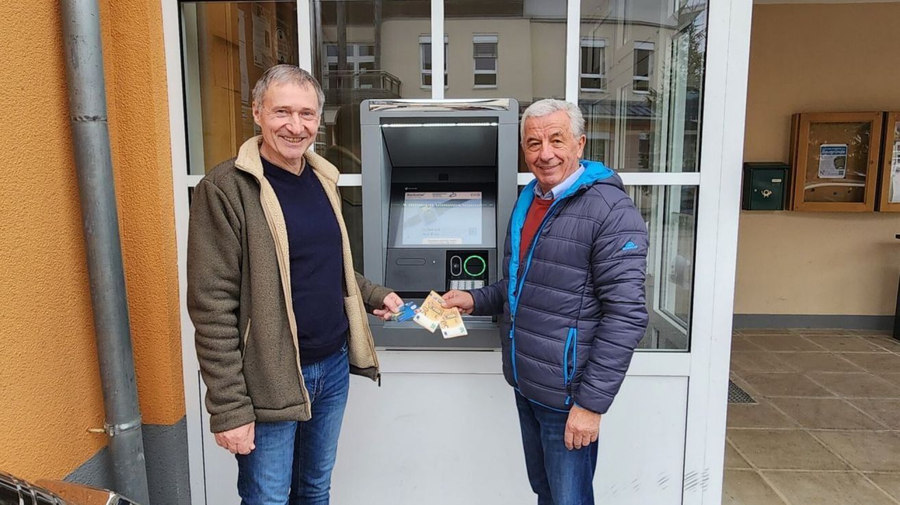 Zwei Männer stehen vor einem Geldautomaten, beide halten Geld in der Hand und lächeln. Ein Mann hat eine Karte in der Hand.